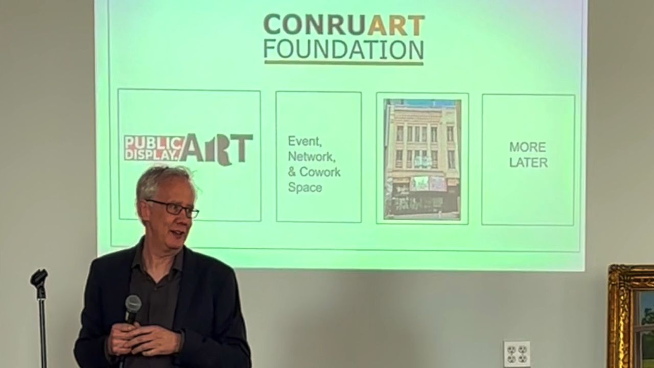 Andrew Conru speaking at a podium in front of a Conru Art Foundation slide
